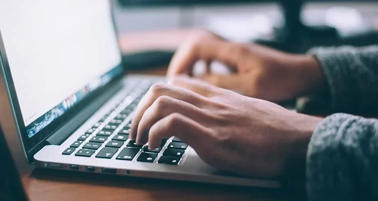 Close-up of a persons hands typing on a laptop keyboard, with a soft focus background and natural light.